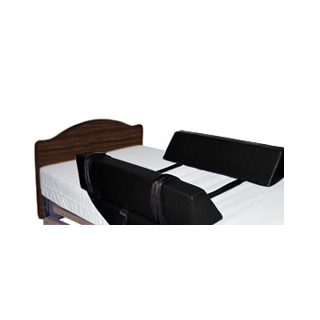 A bed with white sheets and a dark wood headboard features the Proactive Protekt® Roll Control Bolster – Bed Anti-Roll Wedges, secured with straps as a side rail alternative to help keep a person safely positioned while in bed.